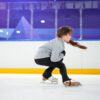 A young girl focuses intently as she practices ice skating indoors.