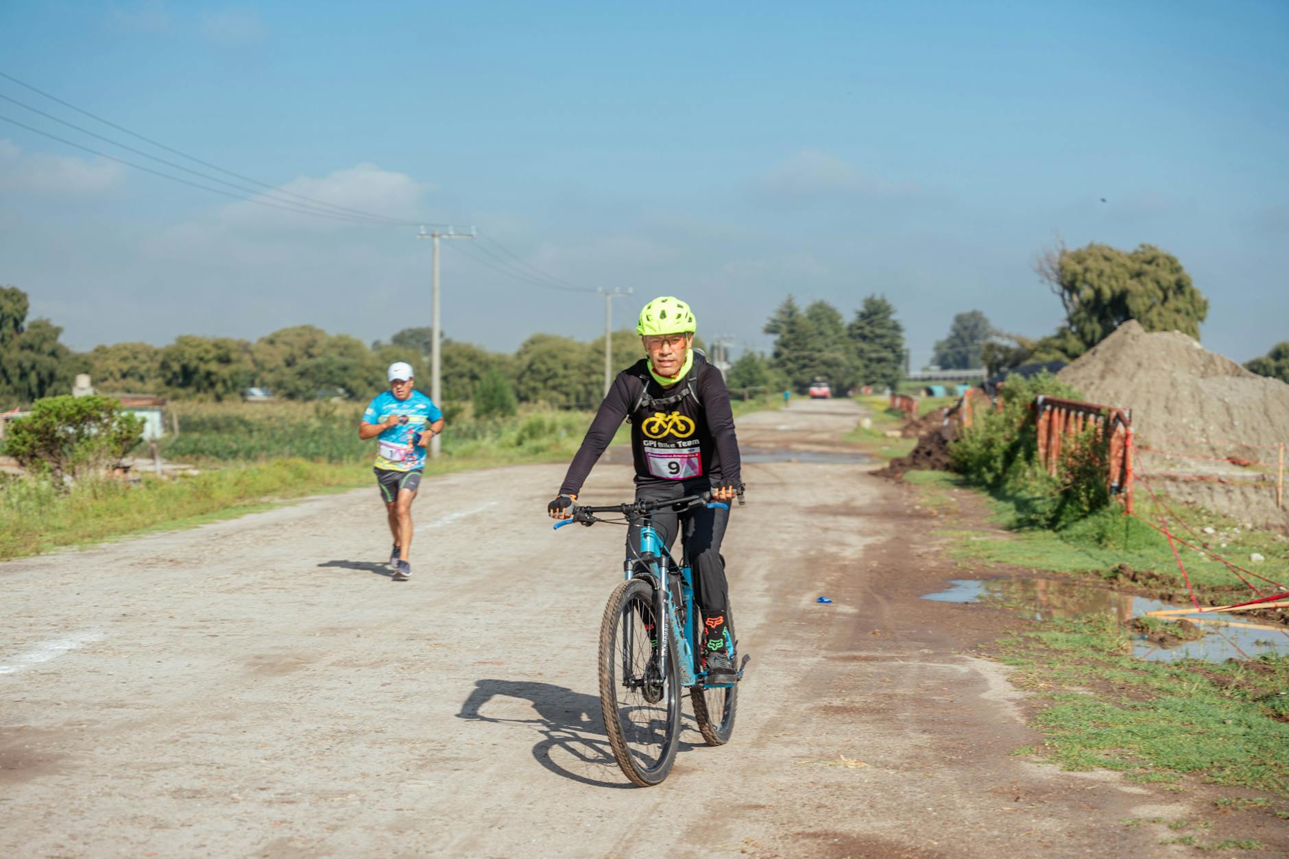 Cyclist and runner participating in outdoor rural race on dirt road.