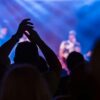 Energetic crowd at a live music concert with vibrant lighting and clapping hands.