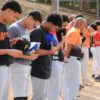 Baseball players lined up with caps off during a pre-game national anthem ceremony outdoors.