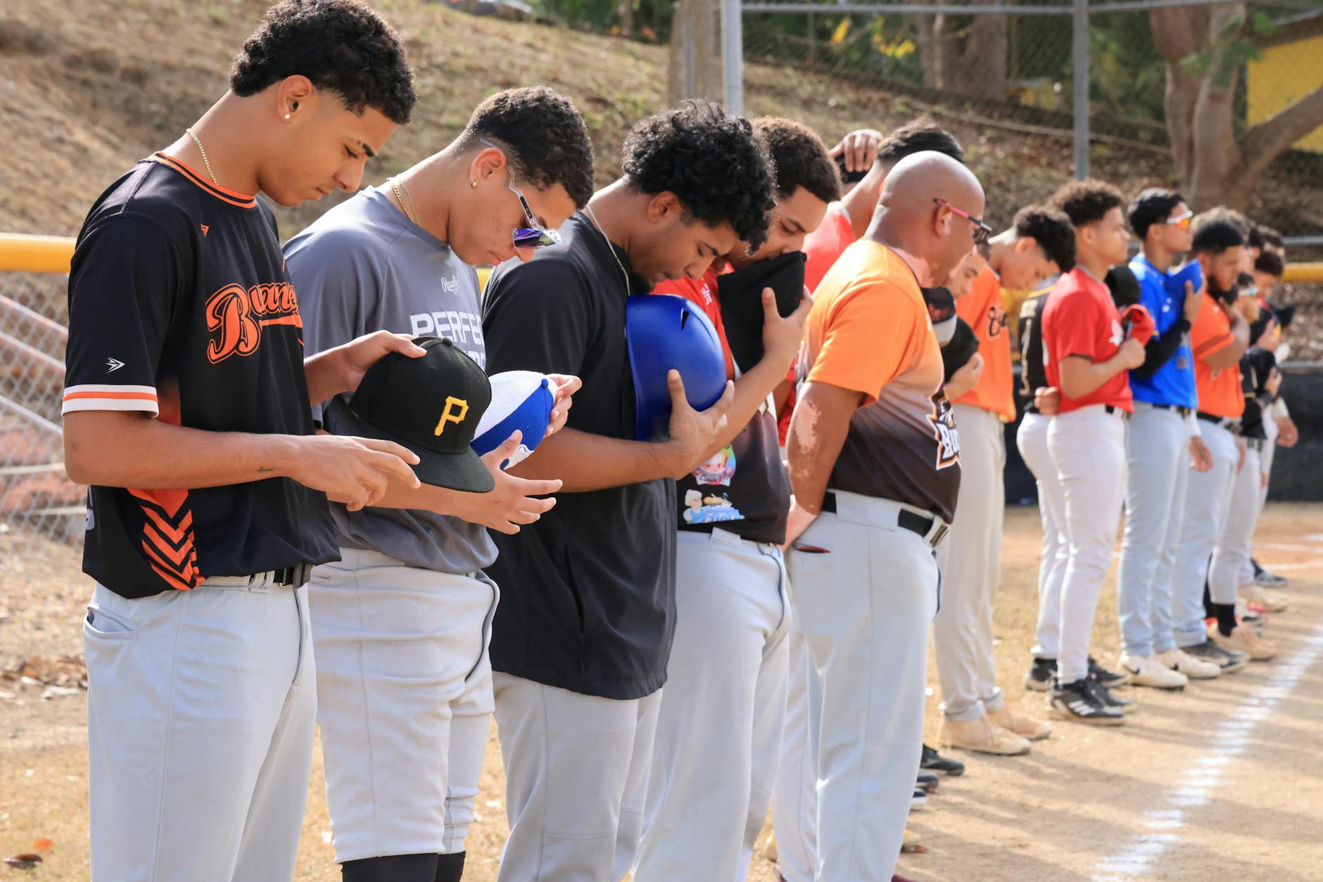 Baseball players lined up with caps off during a pre-game national anthem ceremony outdoors.