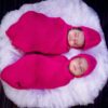 Charming image of twin babies peacefully sleeping in pink knit swaddles on a fluffy surface.