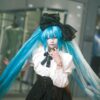 A cosplayer in a detailed anime costume poses confidently in an indoor setting, showcasing vibrant colors and style.