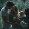 A family enjoying a tender moment together by a peaceful lake surrounded by lush greenery.