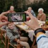 Faceless person with fitness bracelet taking photo with smartphone of big multigenerational family dinner served outside