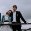 A stylish wedding couple pose against a moody sky, blending formal and casual attire.