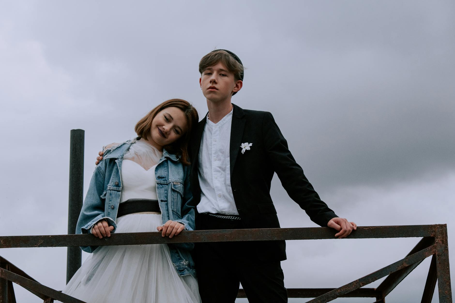 A stylish wedding couple pose against a moody sky, blending formal and casual attire.