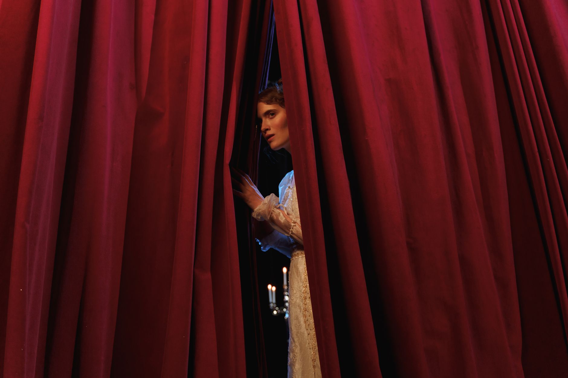 Woman peeks through red theater curtains, capturing a theatrical moment.