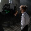 A young actor on a film set, captured in a cinematic moment with professional lighting and camera equipment indoors.