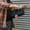Two people in plaid shirts exchanging a fist bump while holding music equipment against a metal backdrop.