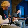 Two musicians playing guitar and bass in an indoor studio setting.