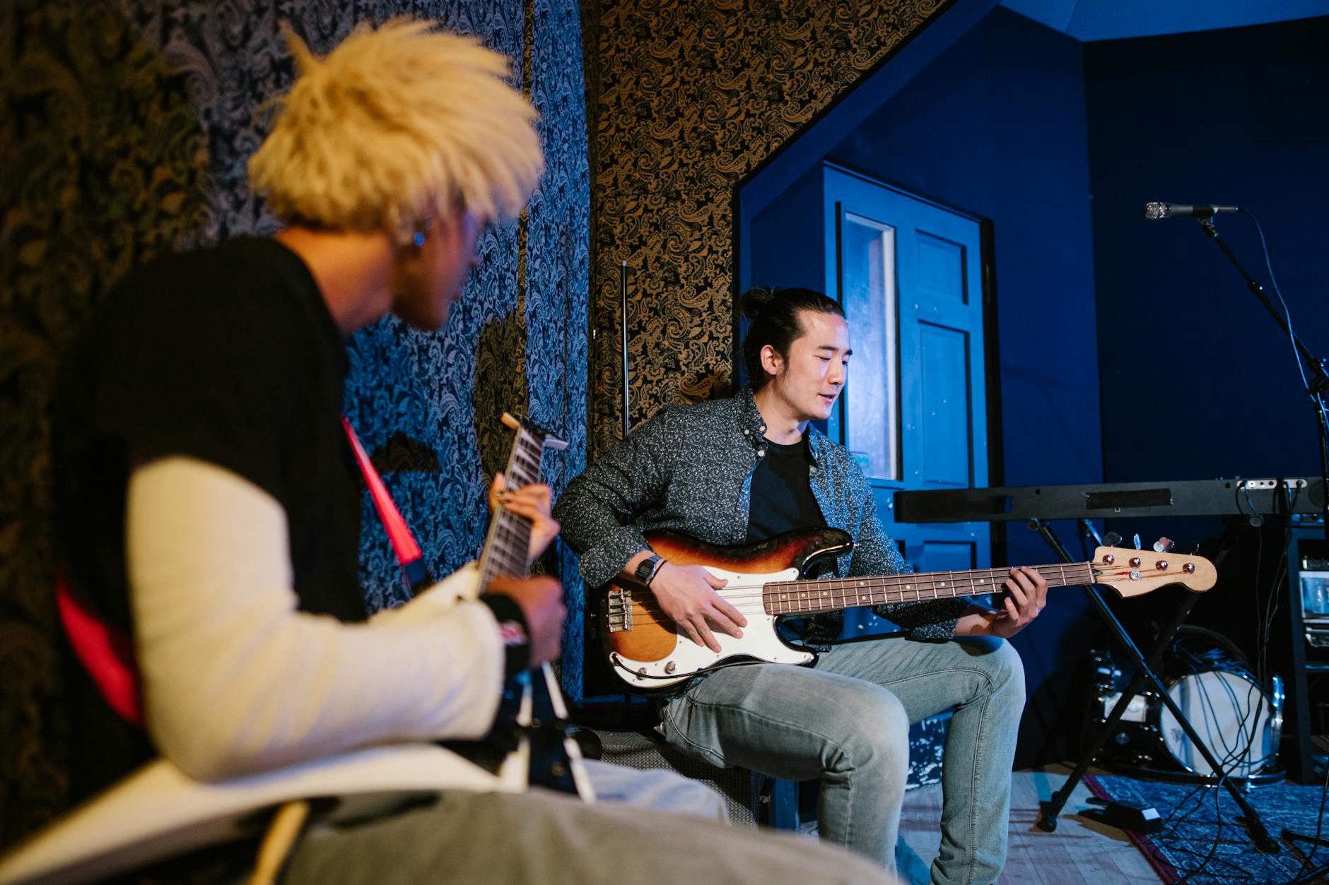 Two musicians playing guitar and bass in an indoor studio setting.