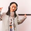 Asian woman singing in recording studio with microphone and headphones, expressing creativity.