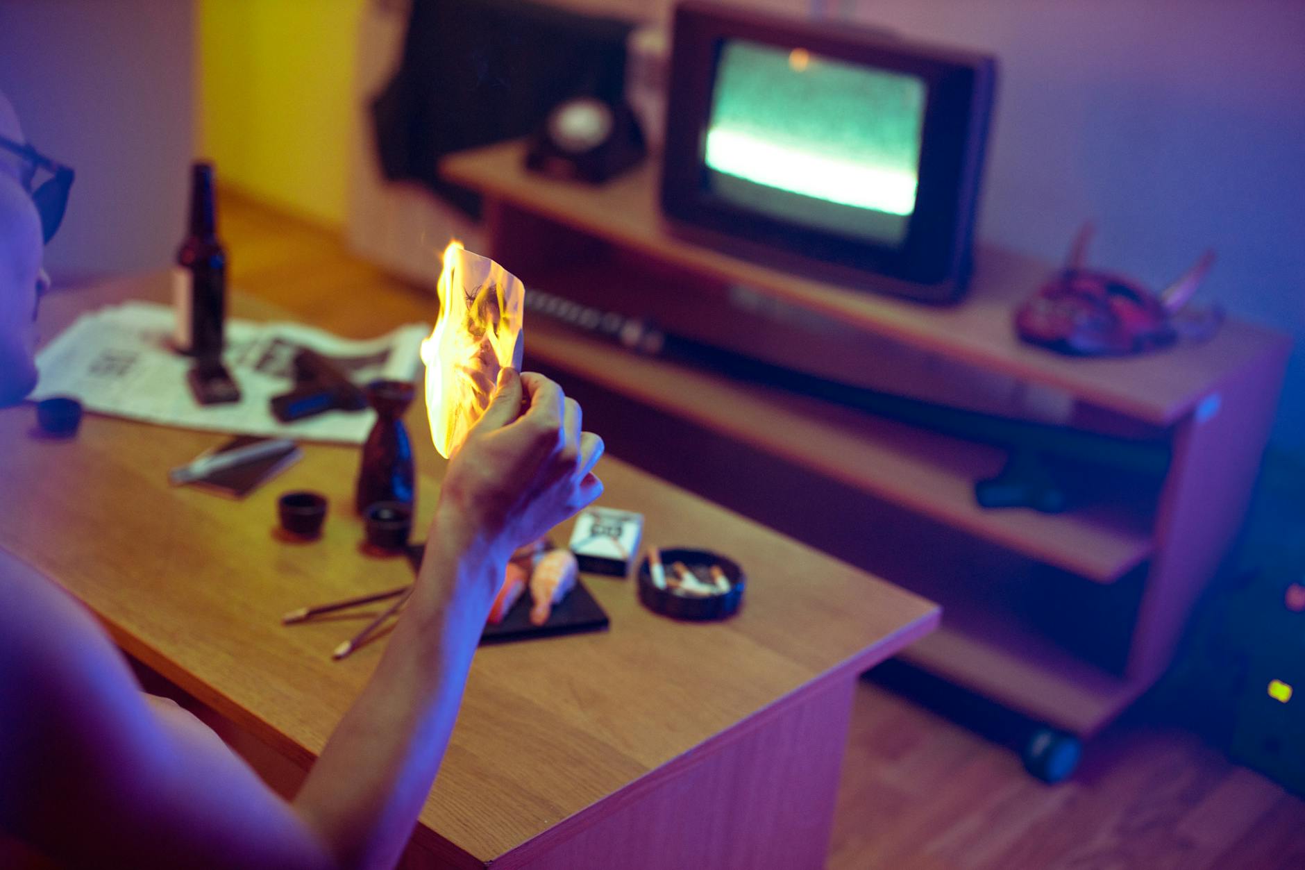 A man burning a photo in a dimly lit room, creating a dramatic and intense atmosphere.