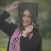 Young graduate woman smiling in cap and gown, celebrating her success outdoors.