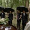 A group mourns during a funeral gathering in a forest cemetery.