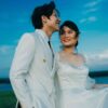 Happy newlywed couple outdoors in elegant wedding attire, radiating joy and romance against a vibrant sky.