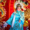 A performer in elaborate traditional attire on a colorful stage with ornate decorations.