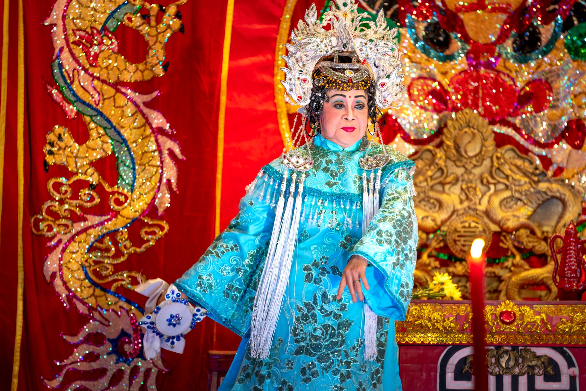 A performer in elaborate traditional attire on a colorful stage with ornate decorations.