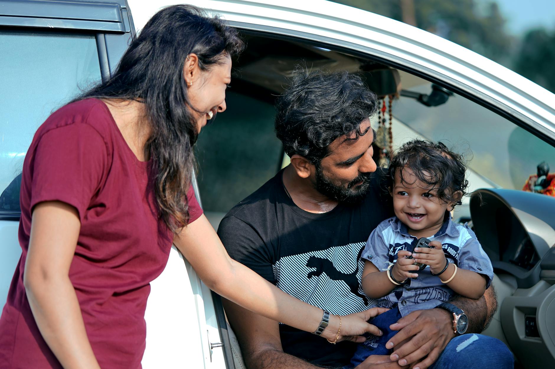 A joyful family moment with parents and child sitting in a car in Sanand, India.