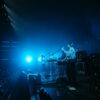 Energetic live band performance on stage with vibrant blue lighting and audience engagement.