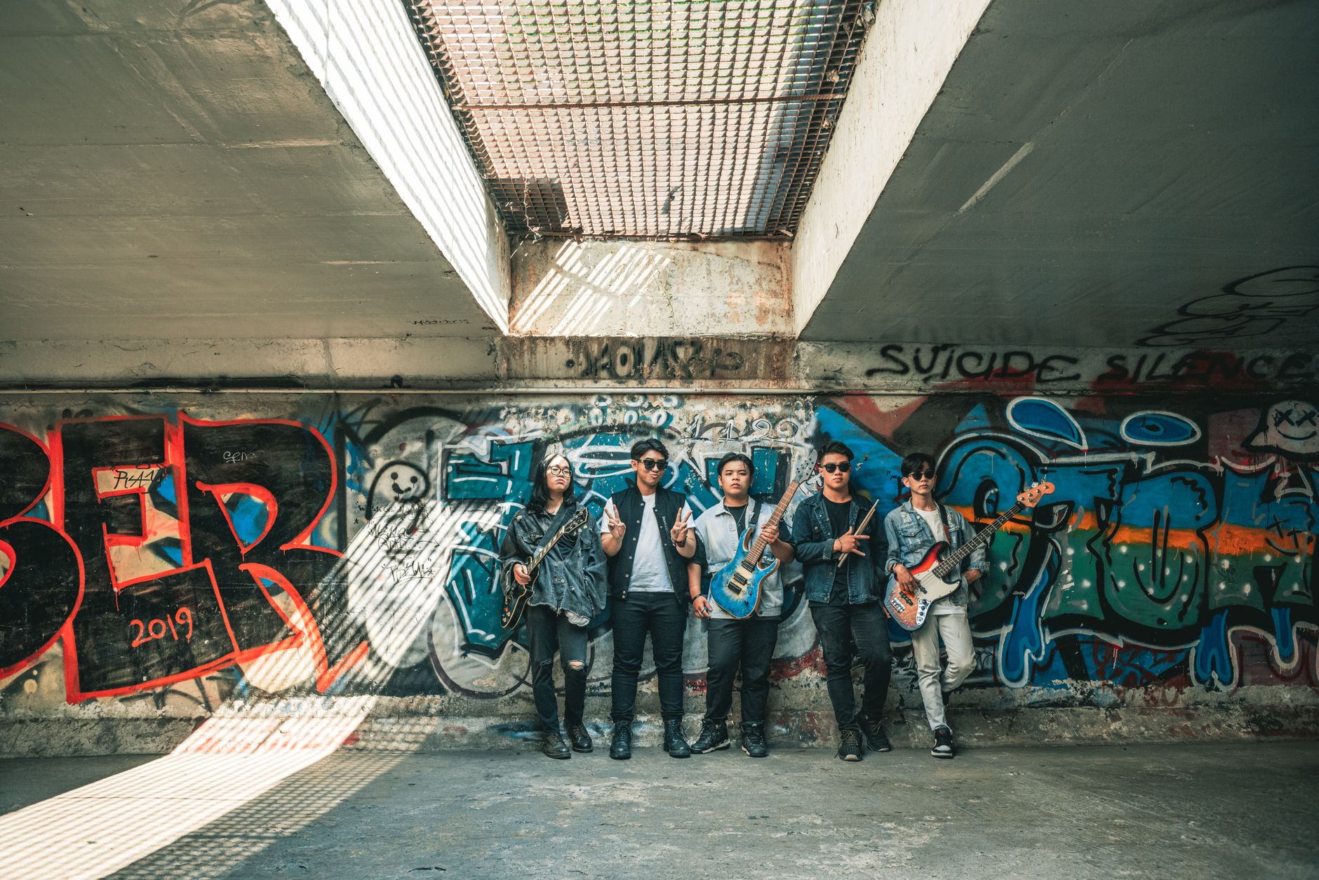 A group of young musicians with guitars standing in front of colorful graffiti in an urban setting.