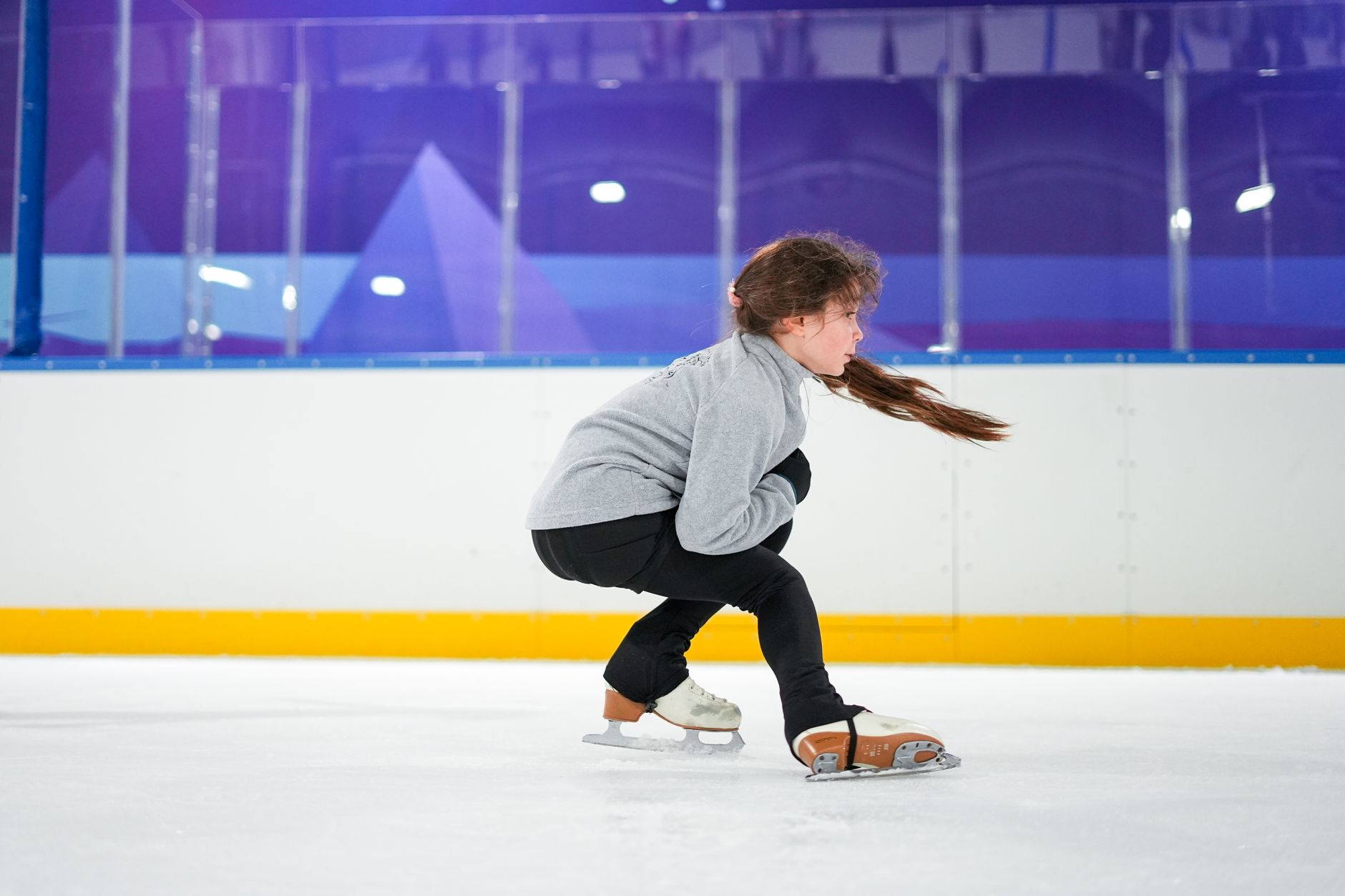 A young girl focuses intently as she practices ice skating indoors.