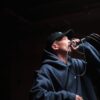 Dynamic shot of a male singer wearing a hoodie and cap, performing at a live concert with a microphone.