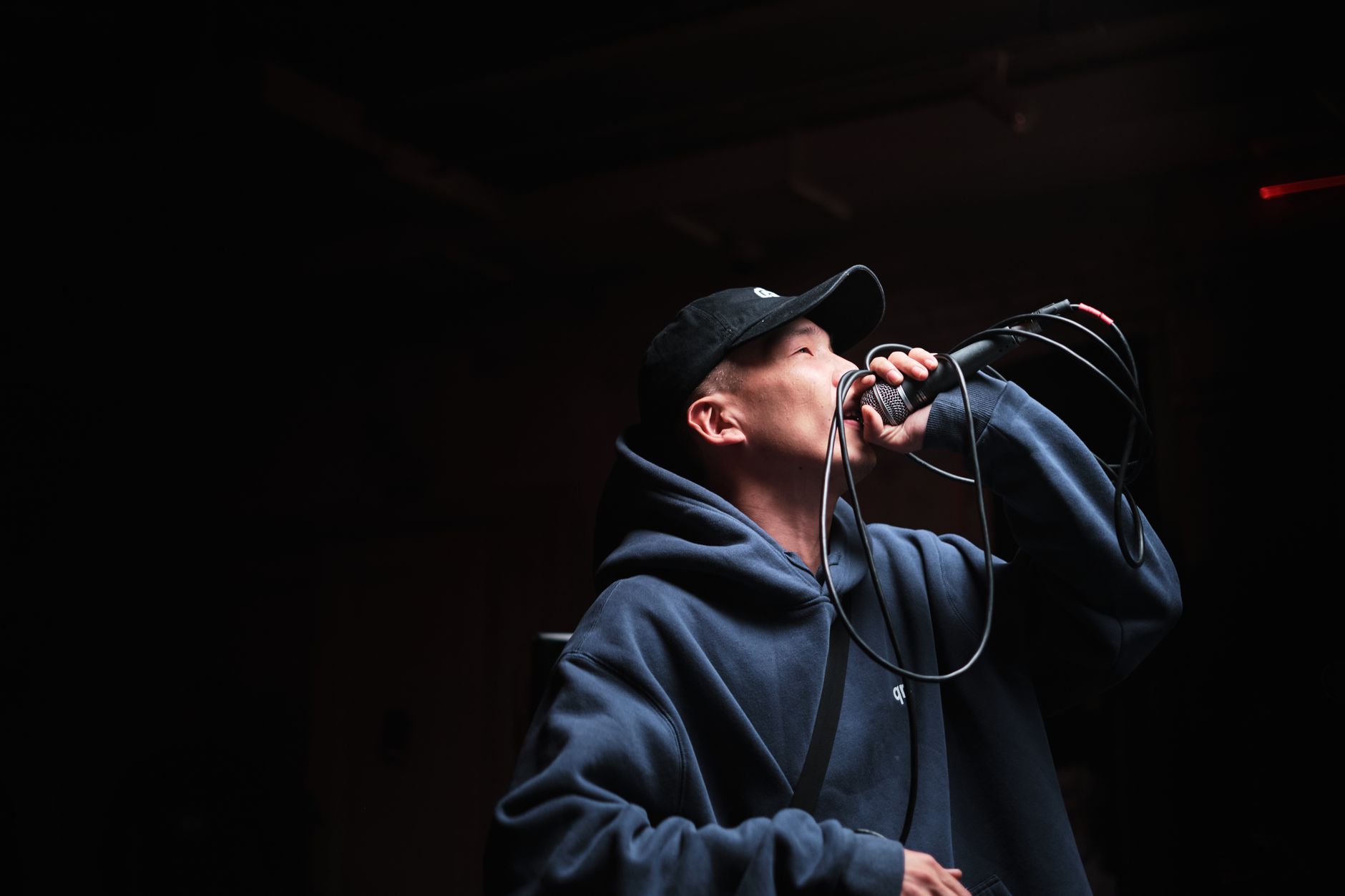 Dynamic shot of a male singer wearing a hoodie and cap, performing at a live concert with a microphone.