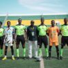 A soccer team with officials posing on a field during daytime at a stadium.