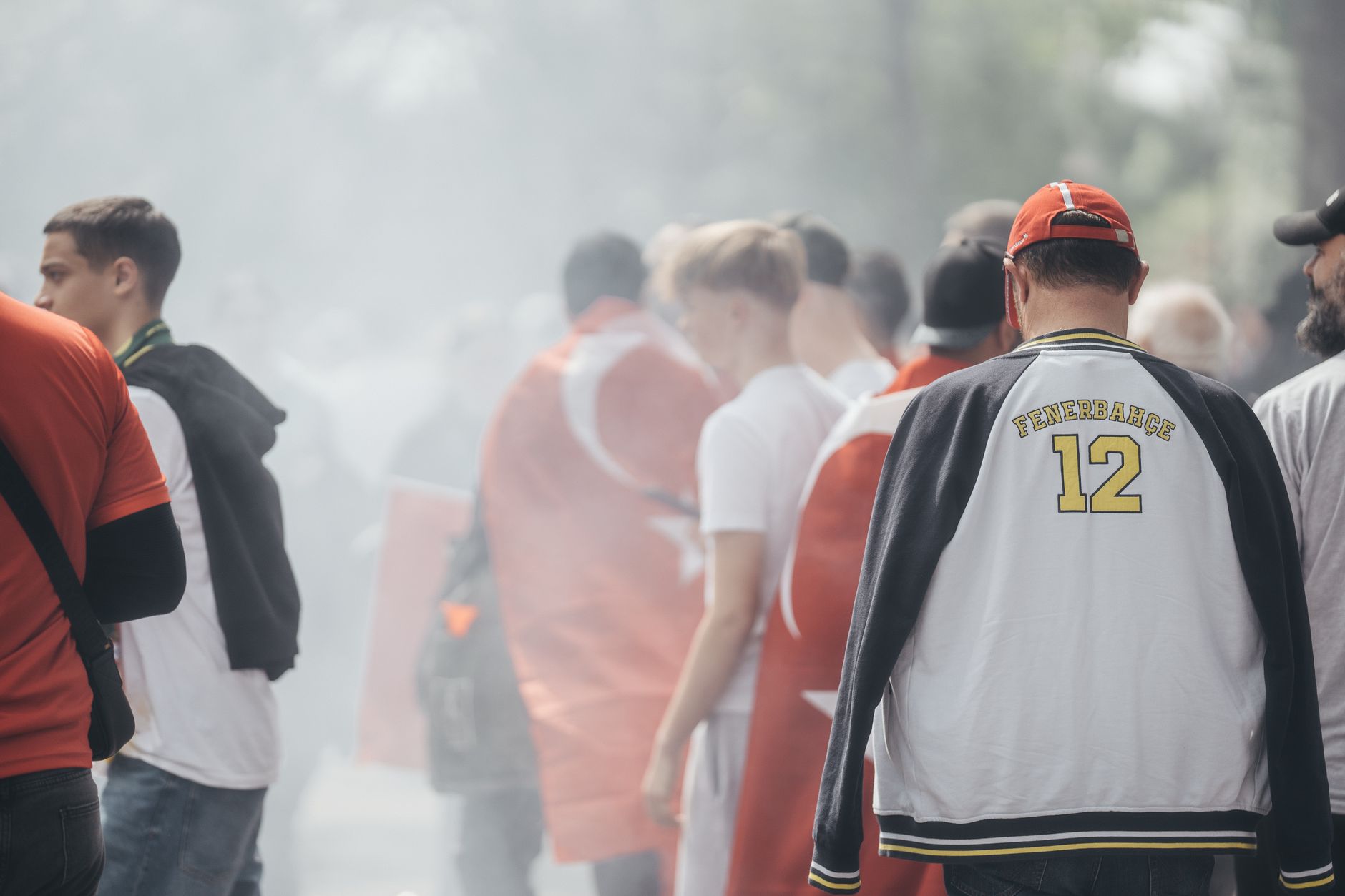 Group of sports fans with Turkish flags and smoke outdoors, showing enthusiasm.