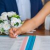 Bride signs marriage certificate during elegant indoor wedding ceremony, symbolizing commitment and togetherness.