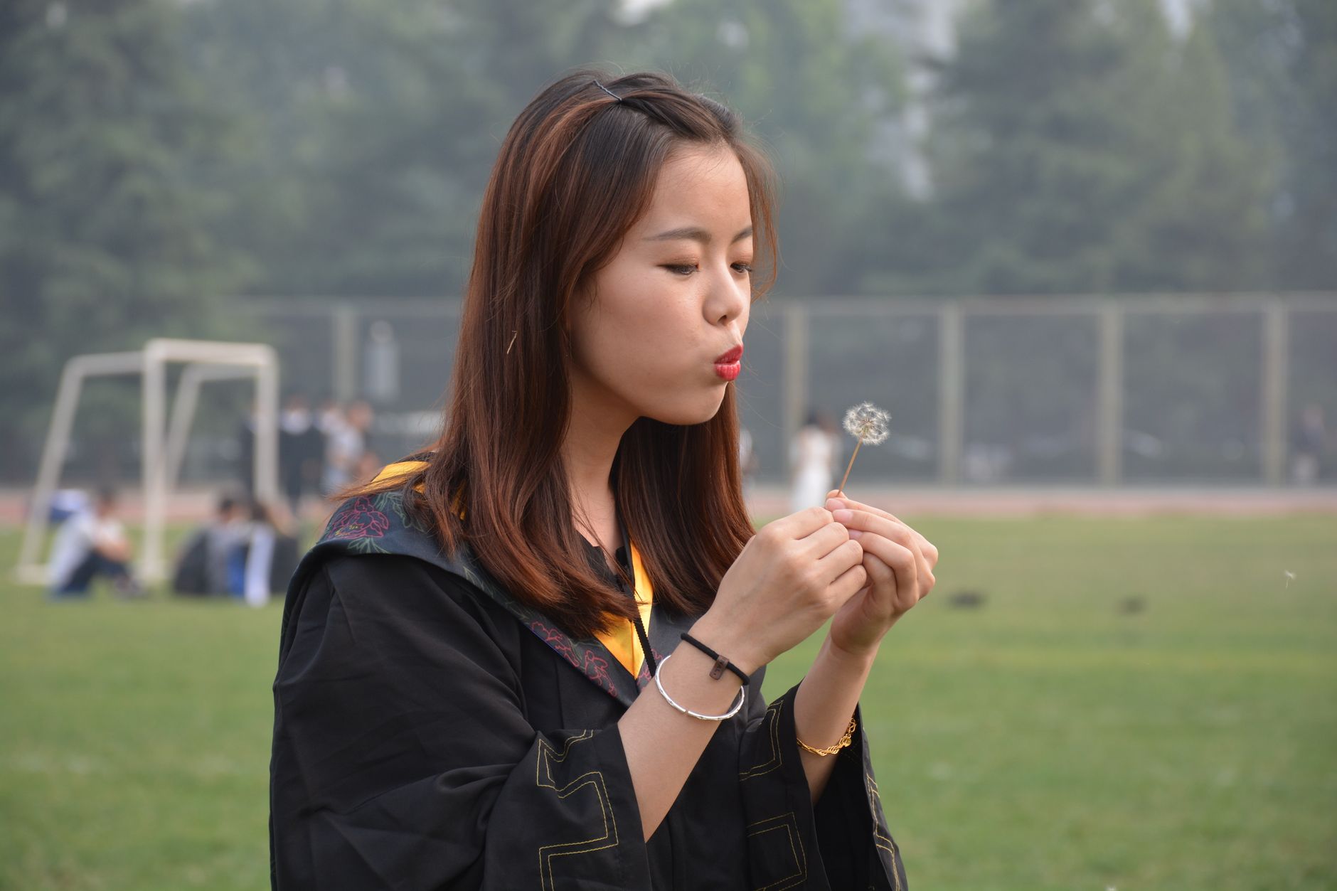 Young graduate celebrates outdoors, making a wish with a dandelion.