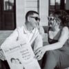 A happy couple sharing their engagement news with sunglasses and newspaper in hand.