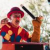 Vibrant clown in colorful outfit entertaining at an outdoor fair.