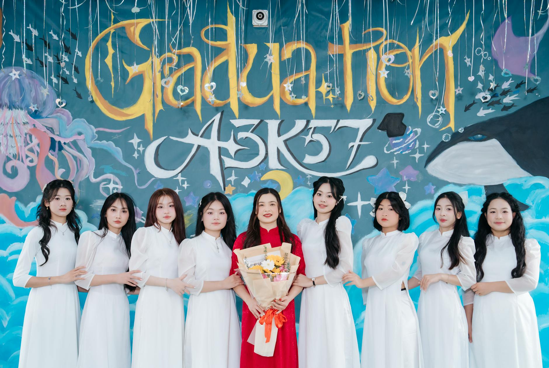Group of graduates posing joyfully in front of colorful graduation mural.