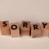 Wooden blocks arranged to spell 'Sorry' on a light, neutral background.