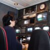 A professional in a TV broadcast control room with multiple screens and equipment.
