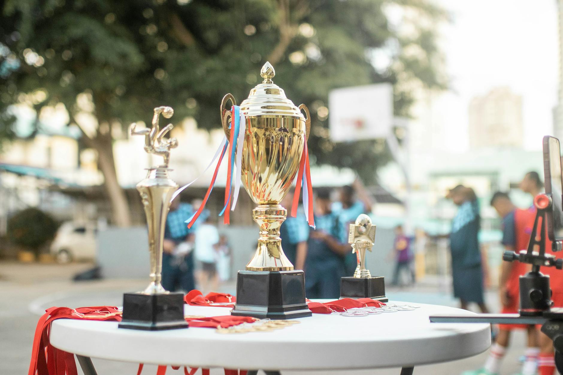 A golden trophy displayed on a table during an outdoor sports event with blurred players in the background.