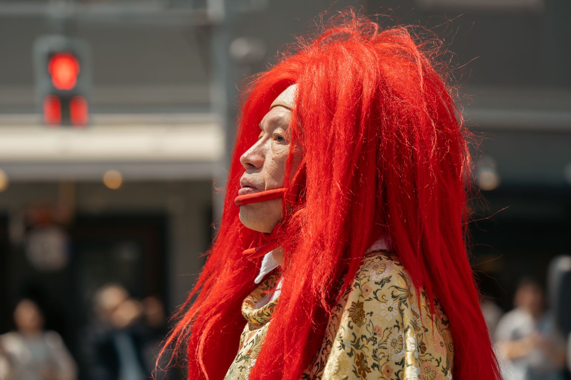 A Japanese performer in vibrant red wig captures attention during a street event in Tokyo.