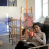 Resting black female in casual outfit sitting on comfortable old armchair and enjoying hot drink while chilling in creative art workspace