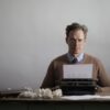 A thoughtful male writer typing on a vintage typewriter, surrounded by crumpled papers.