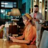 A couple on a first date at a modern café. The woman awaits, using her smartphone.