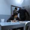 Police officer escorting suspect as lawyer observes during interrogation.
