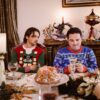 Men enjoying holiday festivities in colorful Christmas sweaters at a lavishly set table.