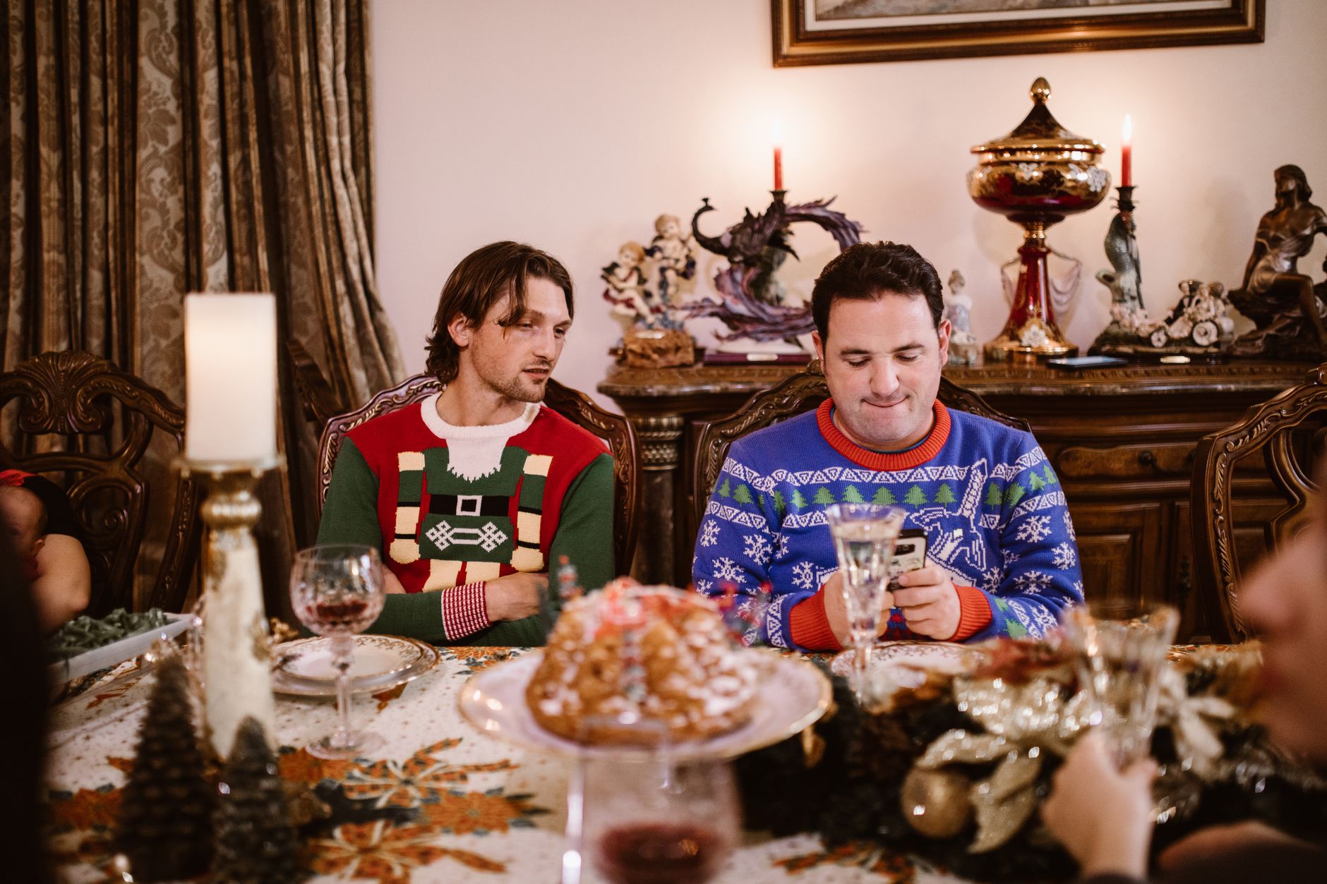 Men enjoying holiday festivities in colorful Christmas sweaters at a lavishly set table.