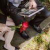 A grieving couple sitting with a red rose and a picture frame in their hands.