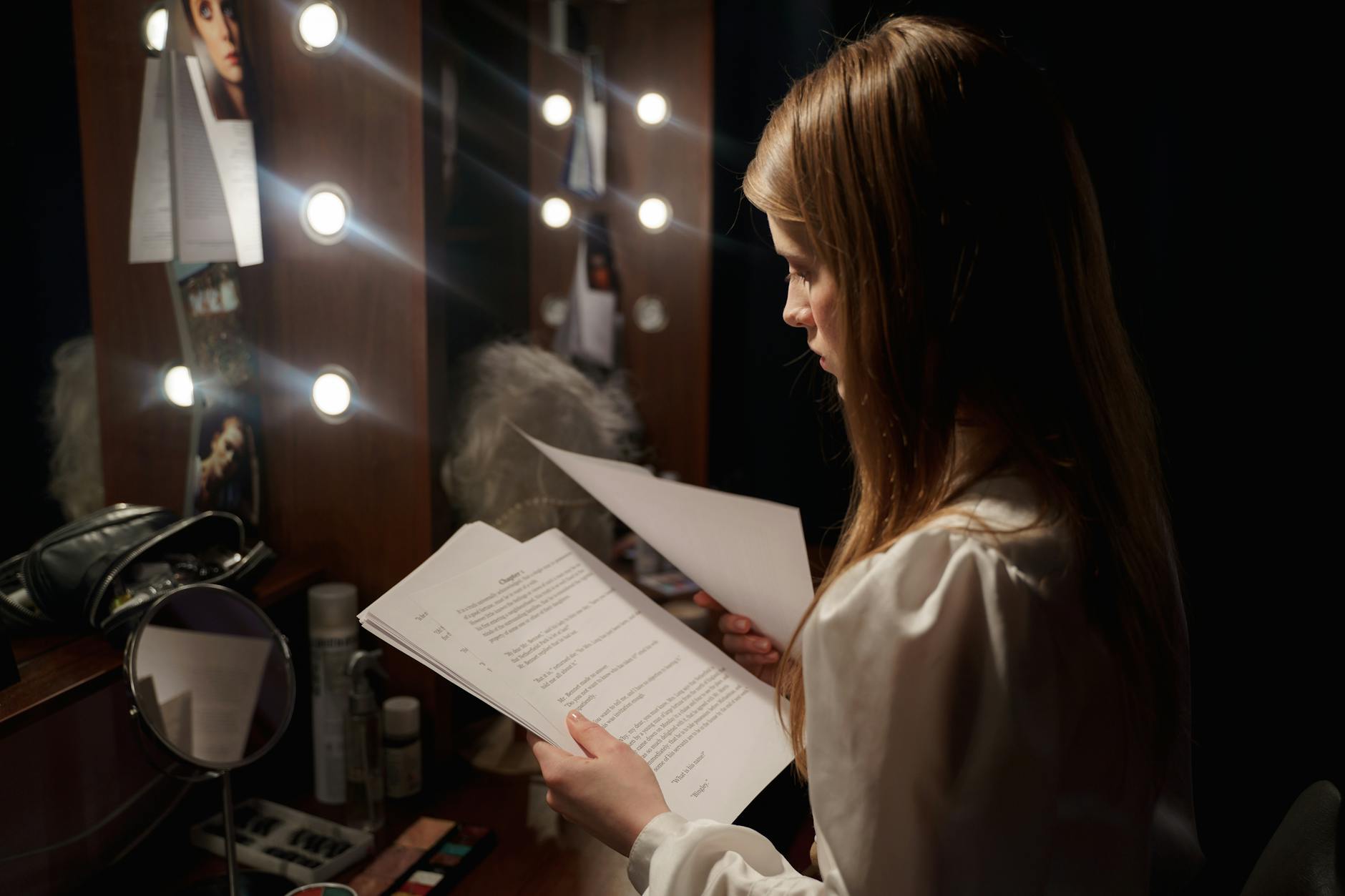 Actress reading script in a dressing room, surrounded by makeup and lights.
