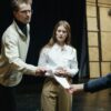 Actors engage in a rehearsal, exchanging scripts on stage, embodying theatrical drama and emotion.