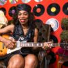 Smiling senior woman enjoying music, playing guitar in a retro-themed room.